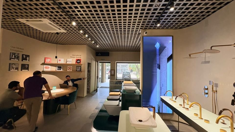 Consultation lounge & fixture gallery. Brushed-gold faucets on a curved counter, a digital display column and a consultation table under the grid ceiling.