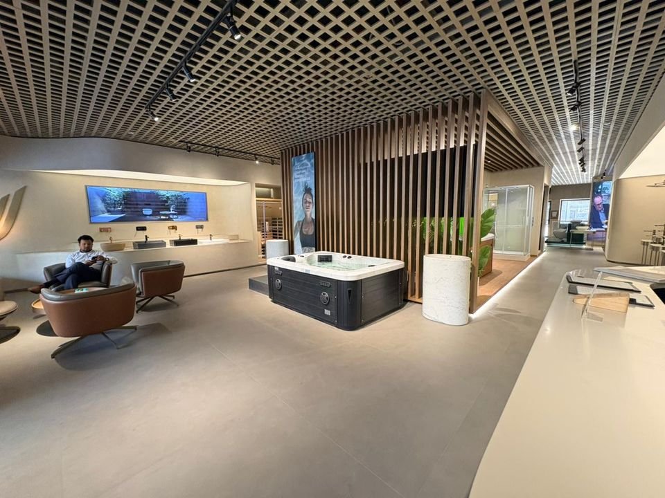 Reception lounge & spa display. Lounge chairs, a spa pool on display and a slatted timber screen beneath the grid ceiling, seen from the reception counter.
