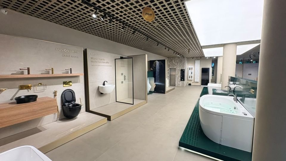 Vanity & whirlpool display. A timber vanity with gold fittings, a black wall-hung WC, a shower bay and a whirlpool bath on a green plinth.