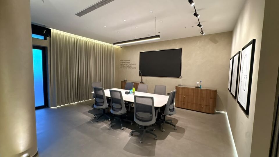 Meeting room. A meeting table, wall display and timber credenza, with a sheer curtain wall and cove lighting.