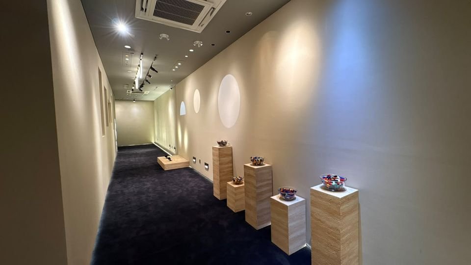 Plinth display corridor. Timber plinths along a softly washed wall with circular light features.
